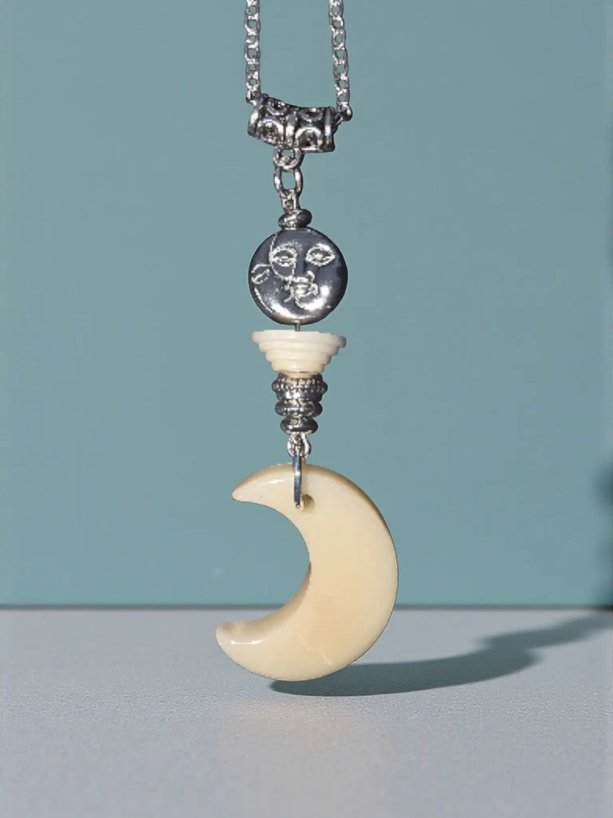 Cream-colored crescent moon shadow necklace with silver face charm and ornate metal accents made from fair trade tagua nut