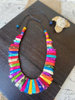 A vibrant tagua nut necklace with glossy multicolored slices in rainbow hues strung on a dark adjustable cord