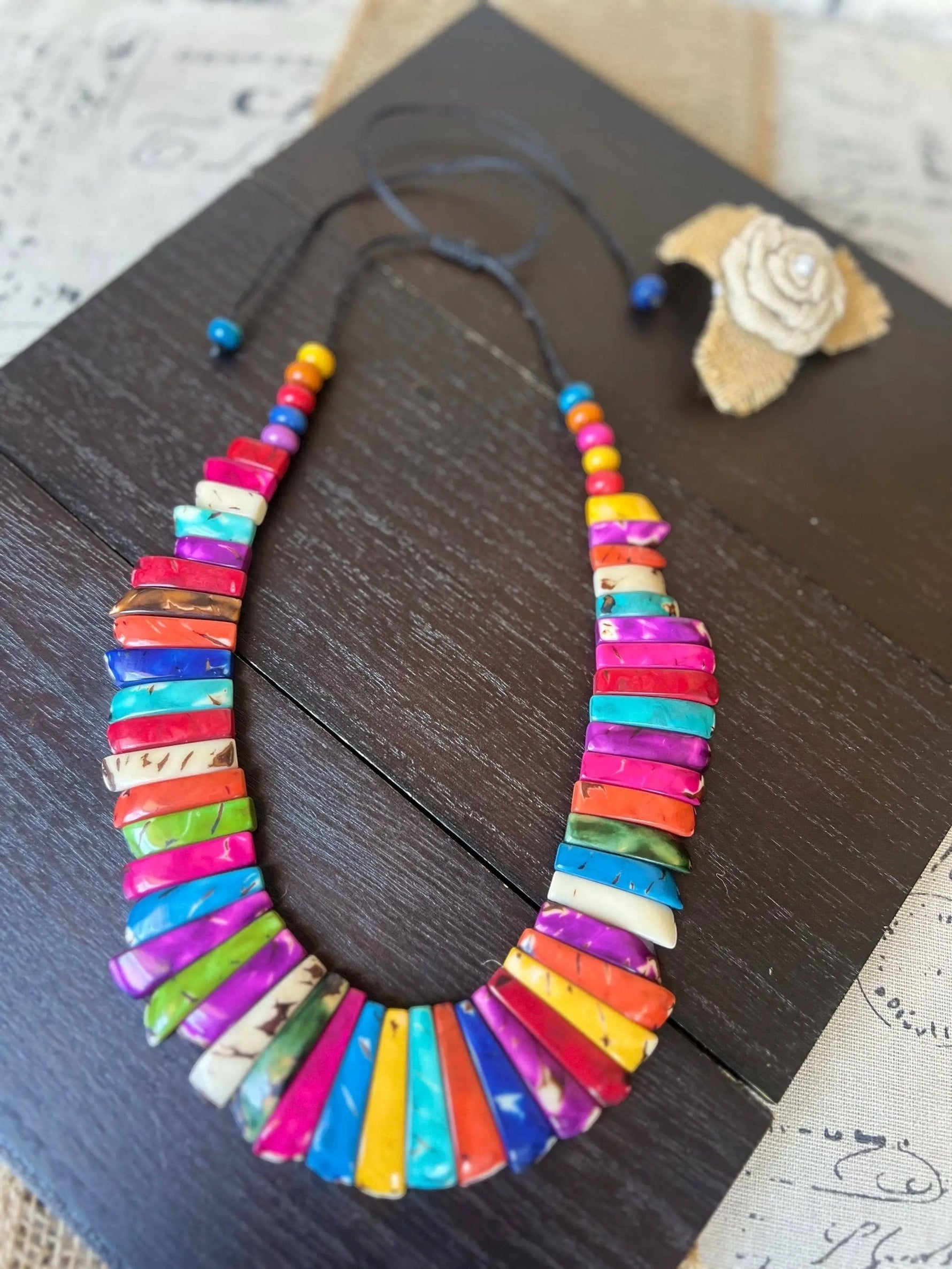 A vibrant tagua nut necklace with glossy multicolored slices in rainbow hues strung on a dark adjustable cord