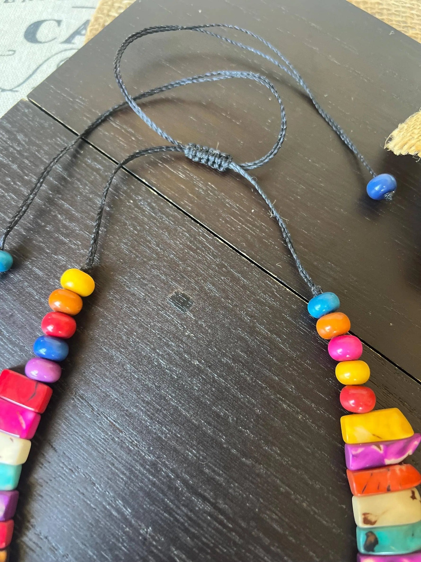 A vibrant tagua nut necklace with multicolored round and rectangular beads on a dark gray adjustable cord