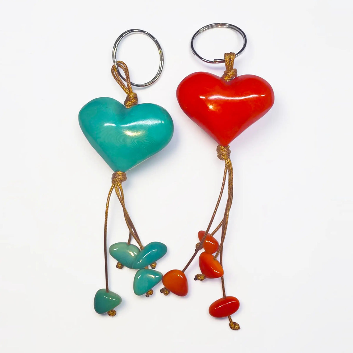 A pair of vibrant red and teal hand carved tagua animal keychains with heart shapes and glossy resin finish on braided cords