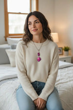 A woman in a cream knit sweater wears a two plum purple tagua nut vegetable ivory necklace with leaf bead