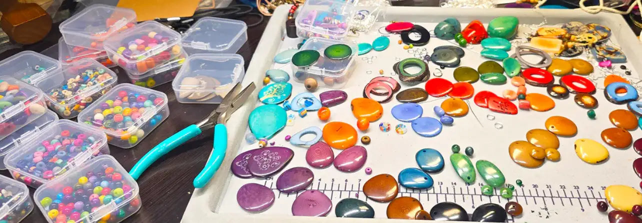 A vibrant collection of colorful, glossy gemstone beads and pendants scattered across a white tray.