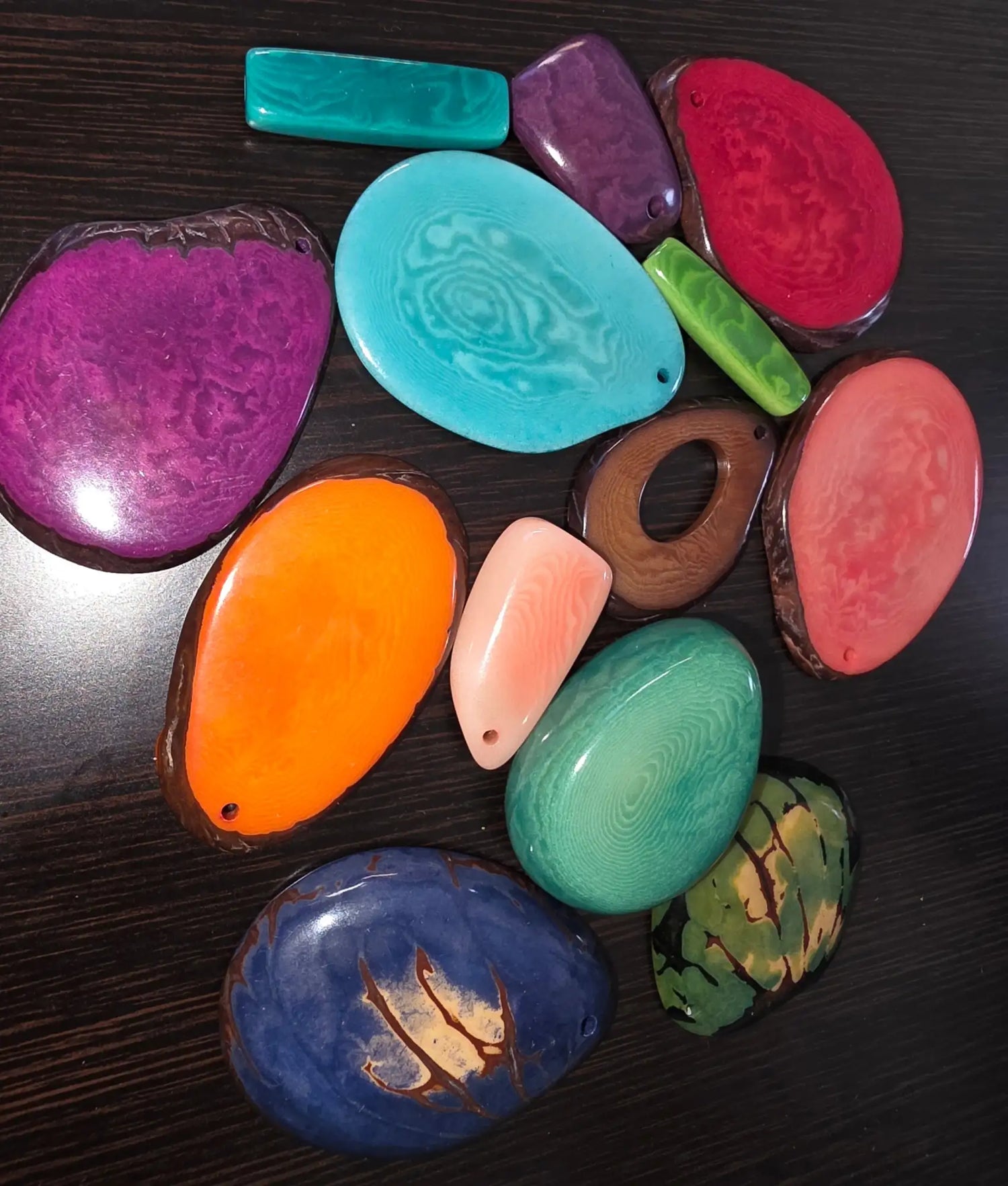 Vibrant, glossy resin pendants in assorted organic shapes and bold colors like purple, teal, orange, green, and blue.