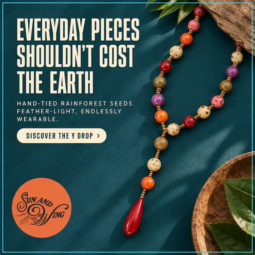 A vibrant, hand-tied necklace featuring colorful rainforest seeds in shades of red, orange, purple, and speckled beige, accented with a glossy crimson teardrop pendant.