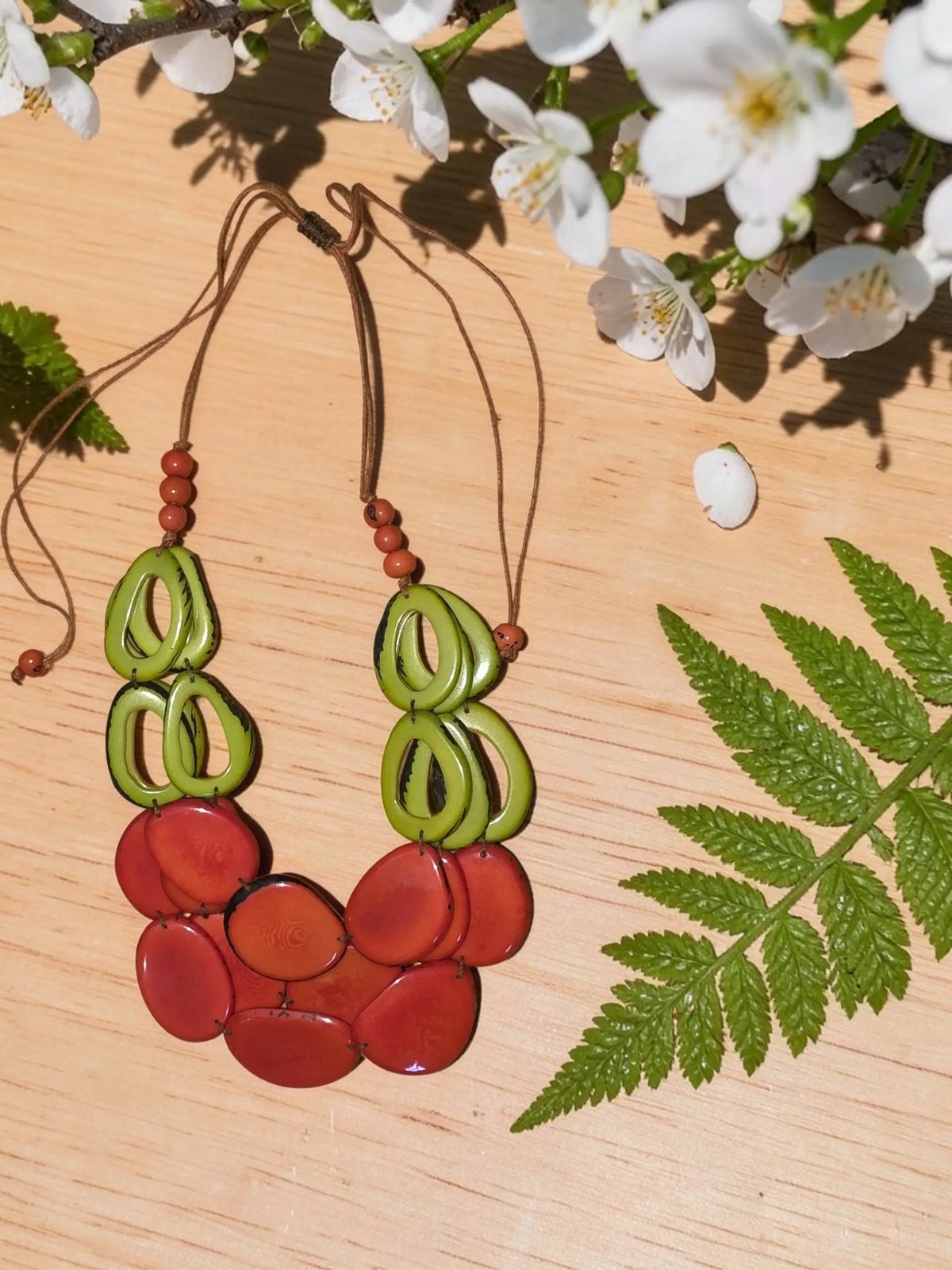 A vibrant handcrafted necklace with layered green and red tagua beads on a natural cord featuring loop accents
