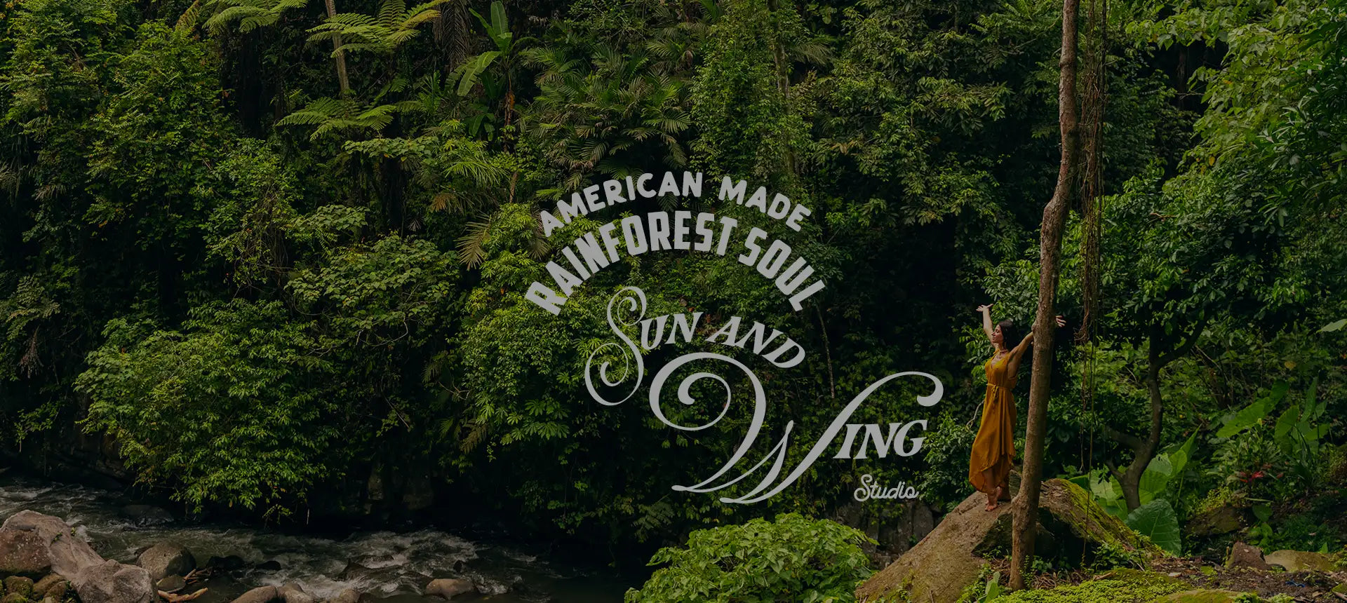 A woman in a flowing golden-yellow dress stands beside a tree, her arms raised as if embracing the lush green forest around her.