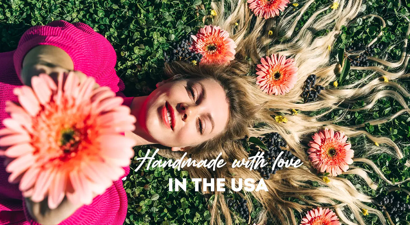 A woman in a vibrant pink knitted sweater lies on green grass, holding a large peach-colored gerbera daisy flower.