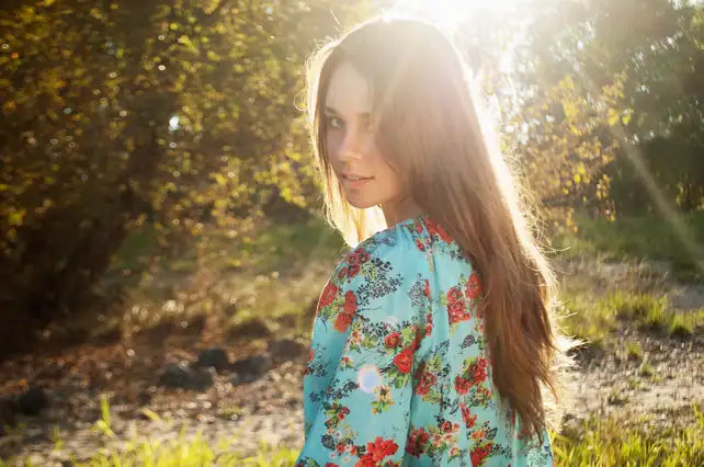 A woman wears a light blue floral dress with red and green blossoms, featuring long sleeves and a soft flowing fabric.