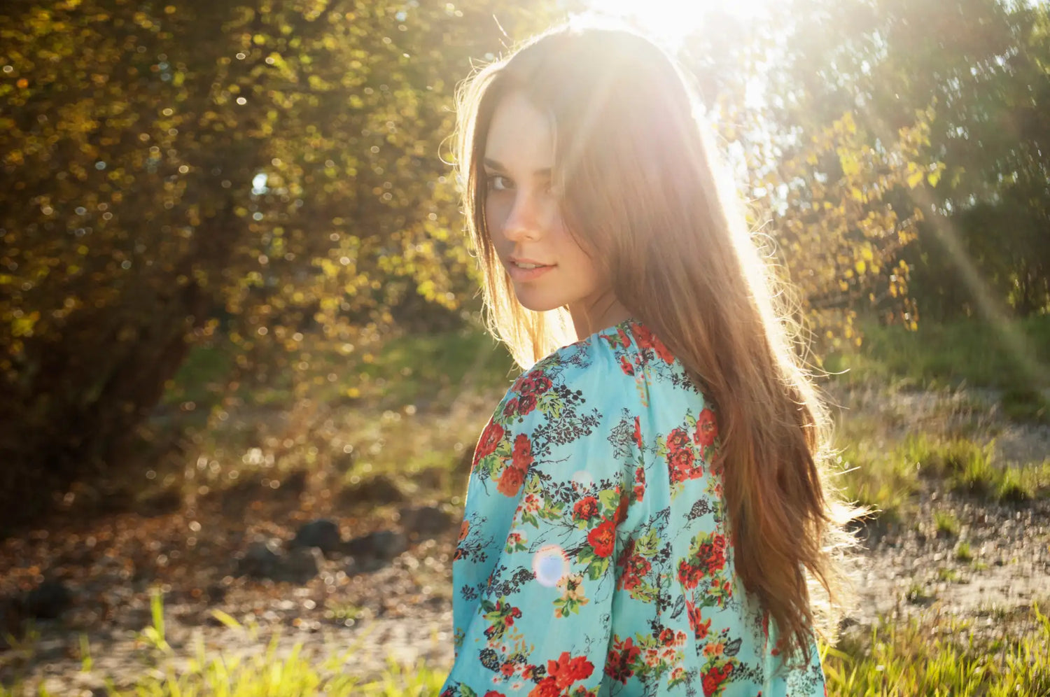 A woman wears a light blue floral dress with red and green blossoms.
