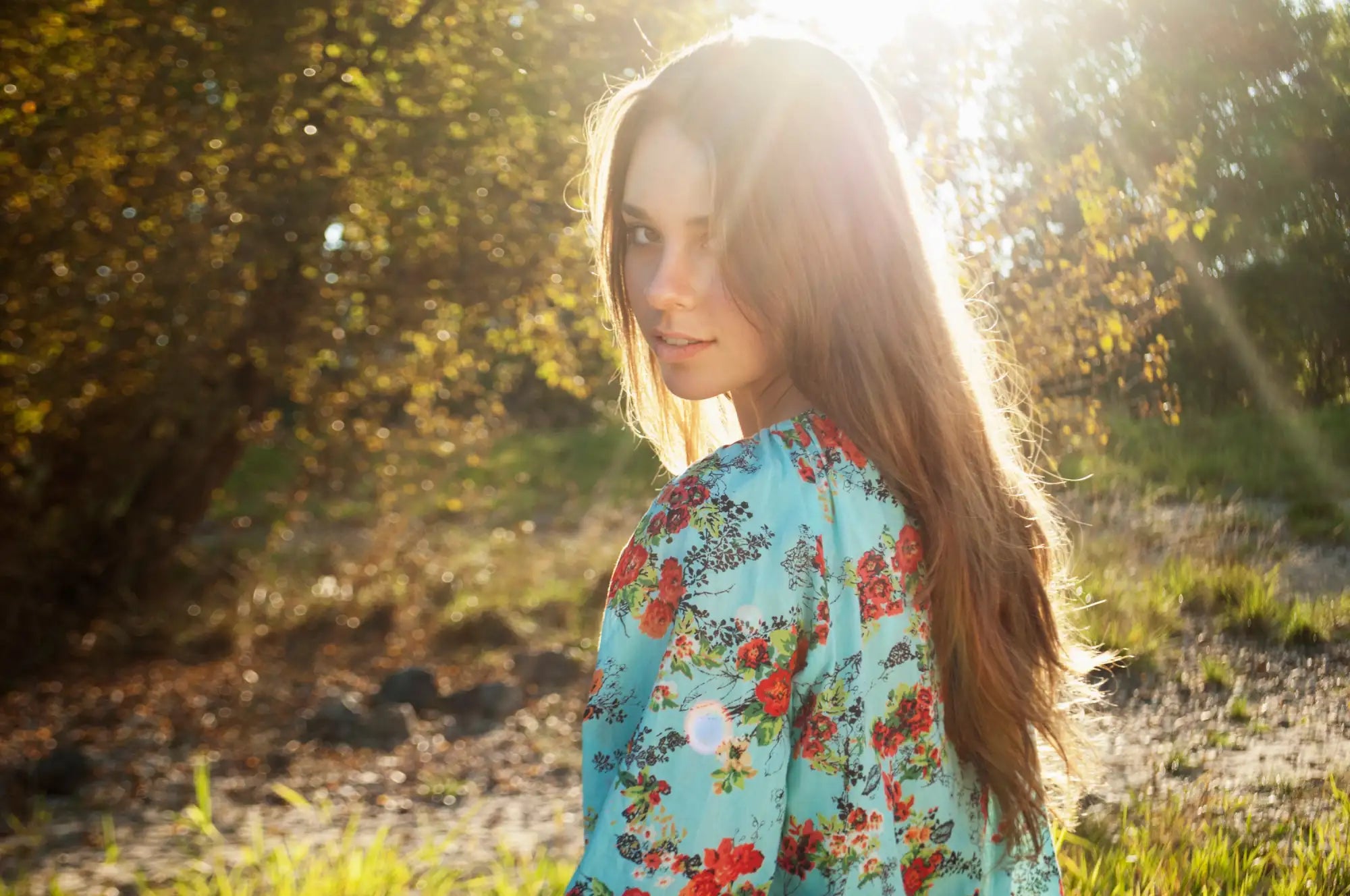 A woman wears a light blue floral dress with red and green blossoms.
