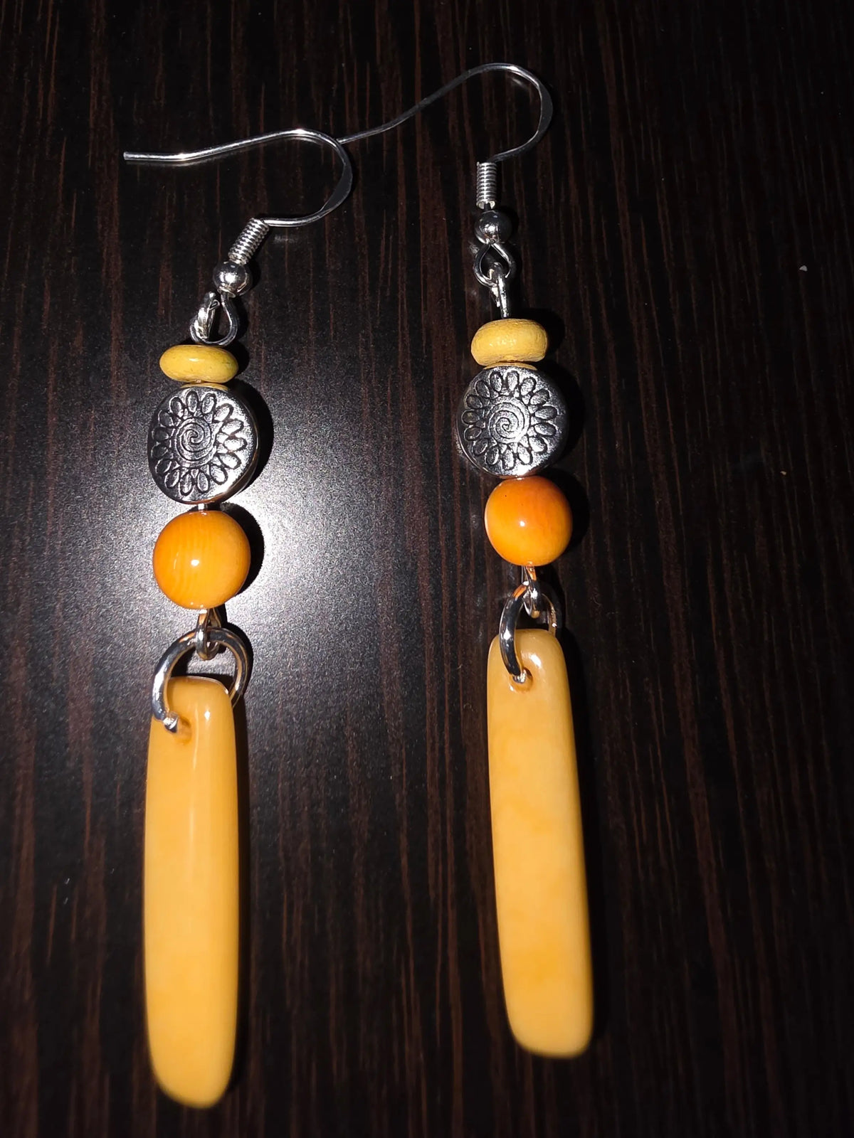 A pair of yellow orange crush baguette tagua earrings with silver hooks, yellow and orange beads, and tibetan amulet sun discs